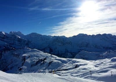 Snow-covered mountains under a clear blue sky with sunlight shining, showcasing a winter landscape ideal for outdoor activities.