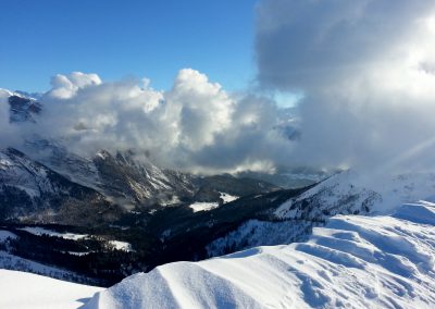 A stunning snowy mountain landscape featuring clouds and a valley, showcasing the beauty of winter scenery in the mountains.