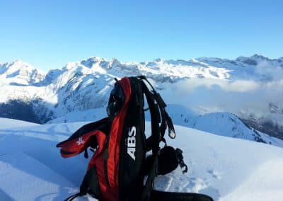 ABS avalanche backpack positioned on snow-covered mountain with scenic peaks in the background, ideal for winter sports enthusiasts.