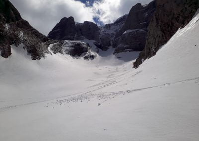 A vast snowy landscape in a mountain valley with rocky peaks and a cloudy sky, showcasing winter scenery and outdoor adventure potential.